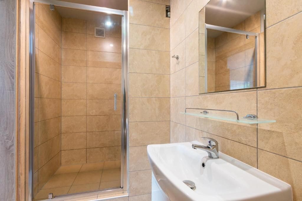 Un baño con ducha, lavamanos y espejo.