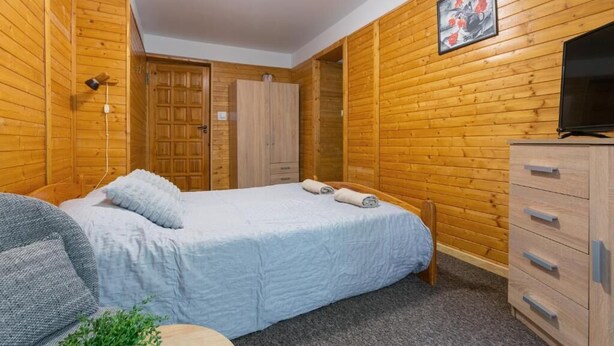 A room with a bed, a wooden wardrobe, a television, and a painting on the wall. - Willa Alaska (Karpacz)