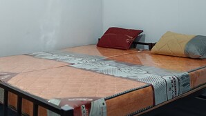 Una habitación pequeña con cama individual, cabecera de madera, almohada roja y almohada amarilla, y colcha estampada.