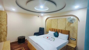 A hotel room with a bed, a chair, a bedside table, a wall-mounted fan, and a ceiling light fixture.