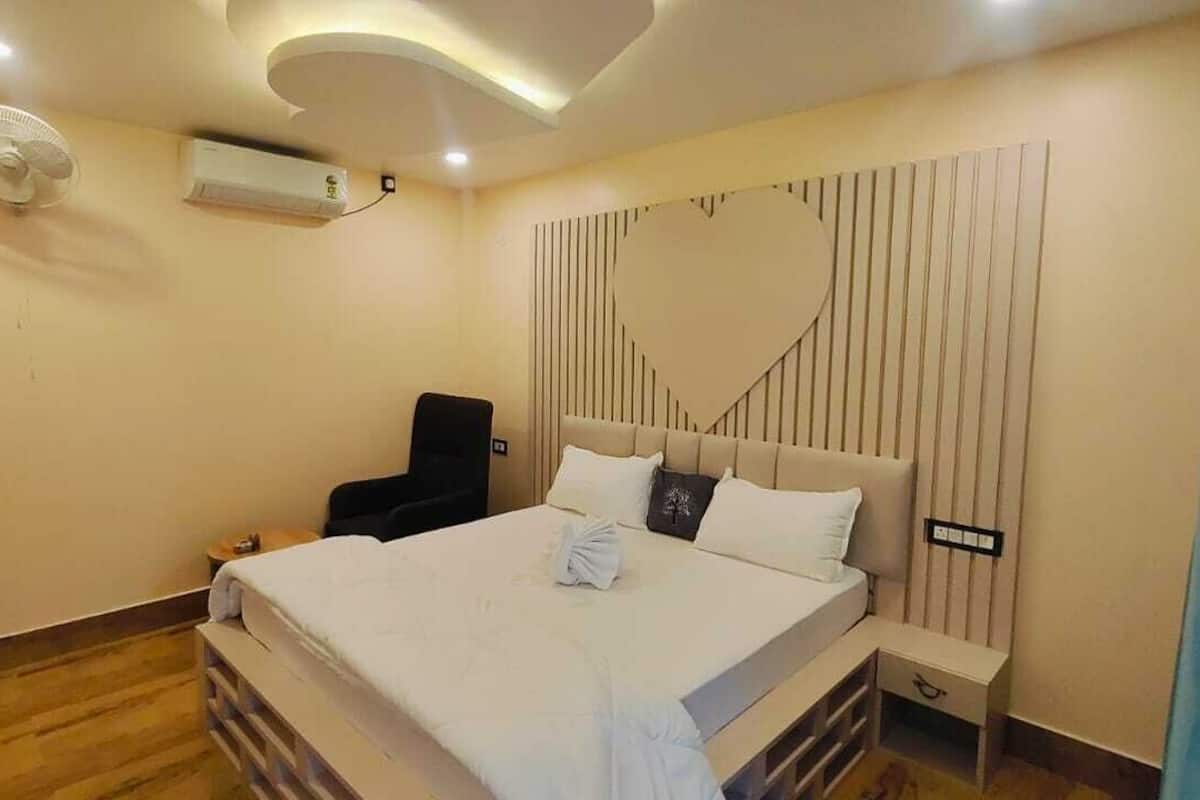 A hotel room with a bed, bedside table, chair, and a wall-mounted air conditioner.
