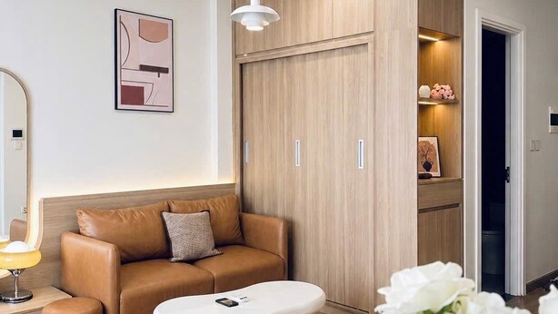 A modern living room with a sofa, ottoman, and a white coffee table. There is a wooden wardrobe with a mirror and a pendant light.