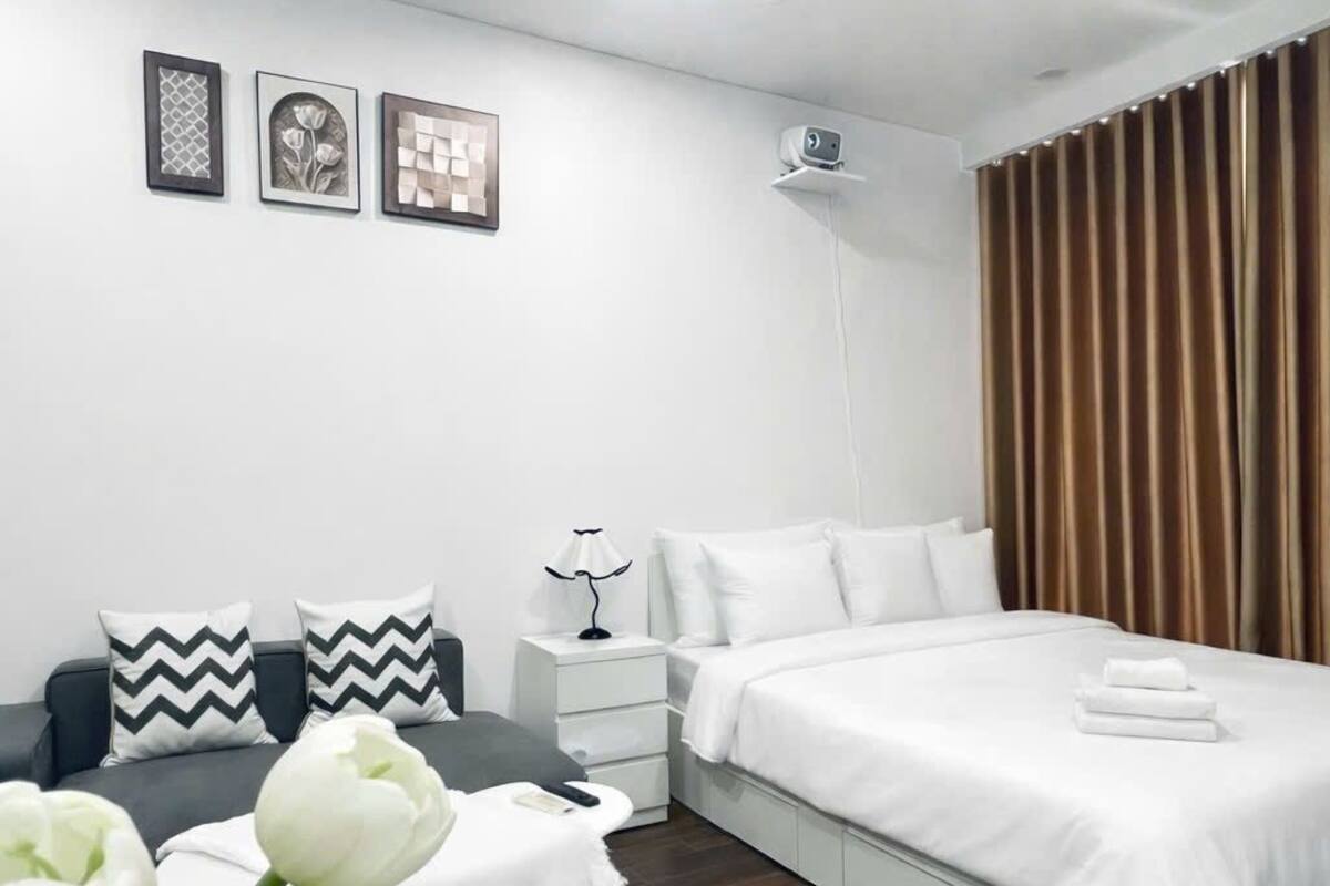 A modern bedroom with a bed, bedside tables, a lamp, and a wall-mounted projector.