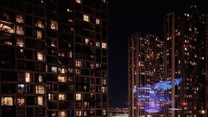 A nighttime view of a high-rise building with illuminated windows, a curved glass structure, and a busy street with cars.