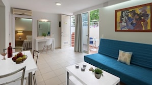 A modern living room with a blue sofa, a dining table with chairs, a small coffee table, and a painting on the wall. - Oliv Apartments (Rethymno)