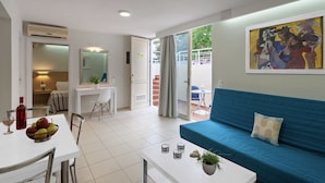 A modern apartment with a dining area, a living room with a blue sofa, a balcony with a table and chairs, and a painting on the wall. - Oliv Apartments (Rethymno)