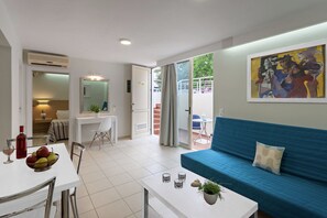 Un apartamento moderno con comedor, sala de estar con un sofá azul, balcón con mesa y sillas, y un cuadro en la pared.