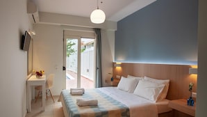 A hotel room with a bed, a desk, a chair, a TV, and a view of the outside. - Oliv Apartments (Rethymno)
