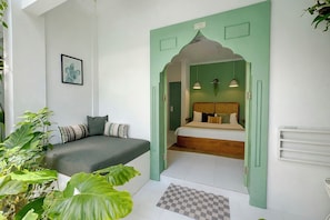 Una habitació amb un llit, una porta verda, una taula petita i una planta.