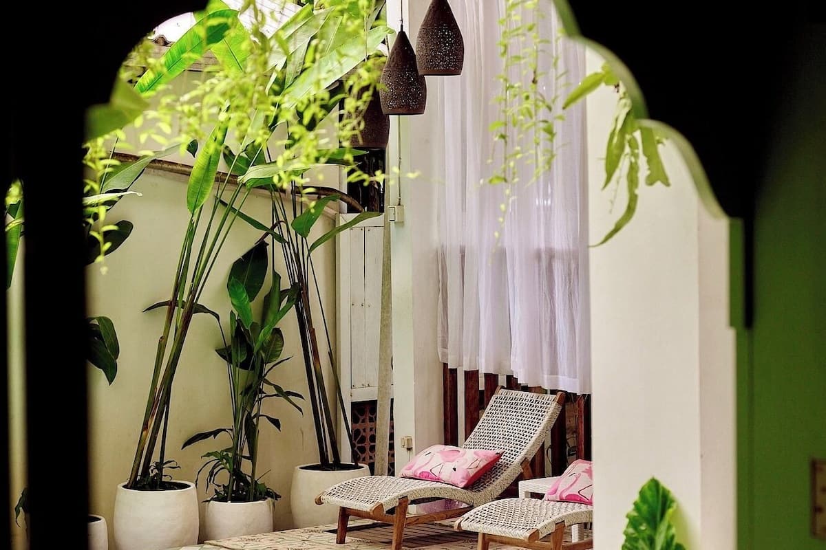 Zona junto a la piscina con sillones de descanso, plantas en macetas y una lámpara colgante.