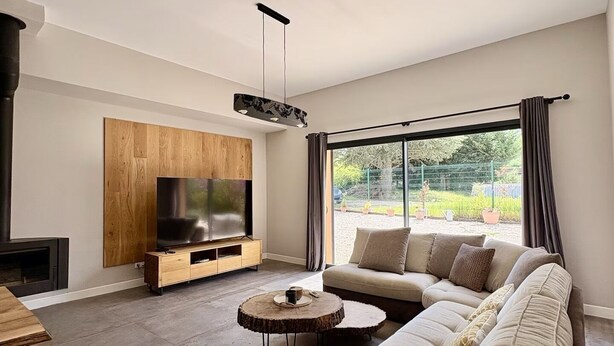 Un salon moderne doté d’un grand téléviseur à écran plat, d’un meuble de rangement en bois, d’un canapé, d’une table basse ronde et offrant une vue sur l’extérieur.