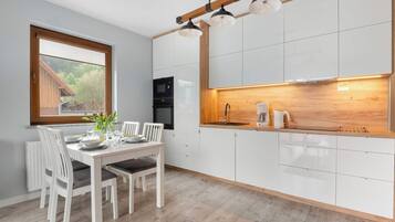 Une cuisine moderne avec des meubles blancs, un plan de travail en bois et un coin repas avec une table dressée pour deux personnes.