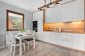 Une cuisine moderne avec des meubles blancs, un plan de travail en bois et un coin repas avec une table dressée pour deux personnes.