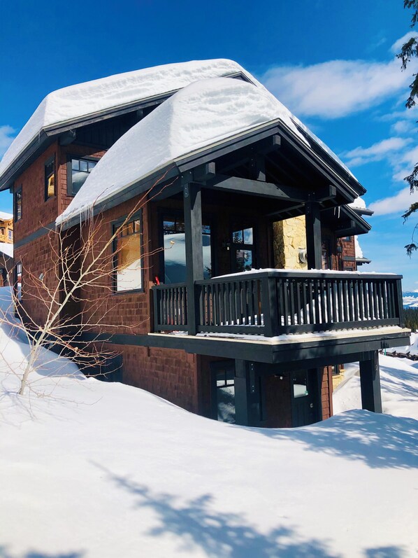 Een houten chalet bedekt met sneeuw, met een balkon en een stenen fundering.