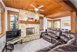 A cozy living room with a stone fireplace, leather sofa, and a television.