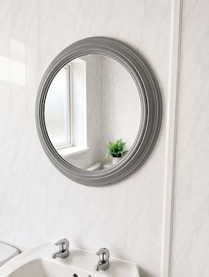 Un baño con espejo redondo, paredes de mármol blanco y una pequeña planta en maceta.