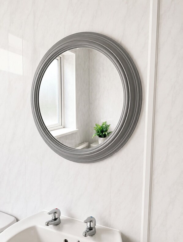 A bathroom with a round mirror, white marble walls, and a sink with two faucets.