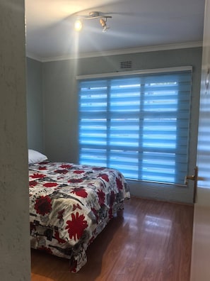 A bedroom with a bed, a window with blinds, and a ceiling light fixture. - Charming 2-Bedroom Apartment in Johannesburg South (Johannesburg South)