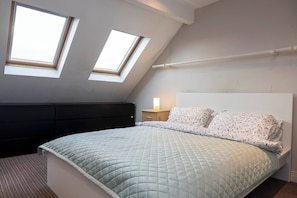 A bedroom with a bed, two skylights, a bedside table with a lamp, and a dark headboard. - Coastal town house beside train and buses only 5 kilometer's from city centre (Blackrock)