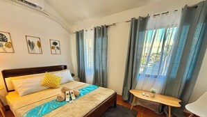 A hotel room with a bed, a small table, a chair, and a window with curtains.