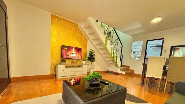A modern living room with a staircase, a flat-screen TV, a sofa, and a coffee table.