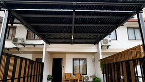 A covered walkway leading to a building with a black roof, a wooden bench, and potted plants.