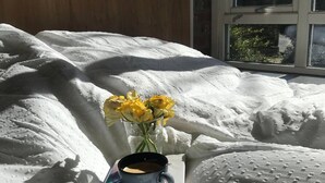 Una cama con una taza de café y flores amarillas sobre una bandeja.