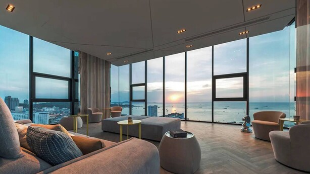 A modern living room with large windows, a sofa, a coffee table, and a view of the ocean and city skyline. - 2 Bed Room Sea View Luxury - Best Location in Pattaya (Muang Pattaya)