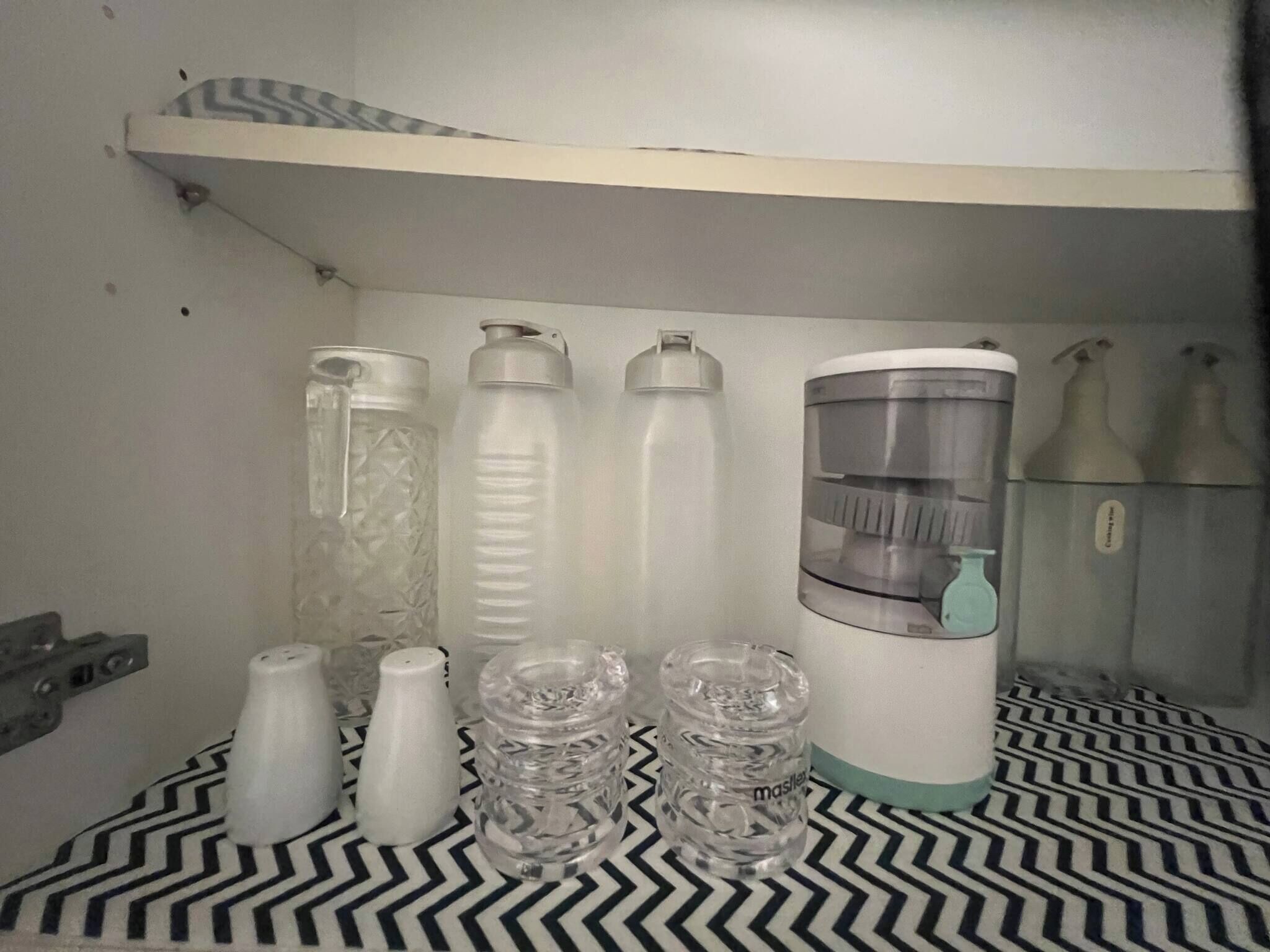 A room with a patterned floor, a shelf with various water bottles, and a coffee maker.