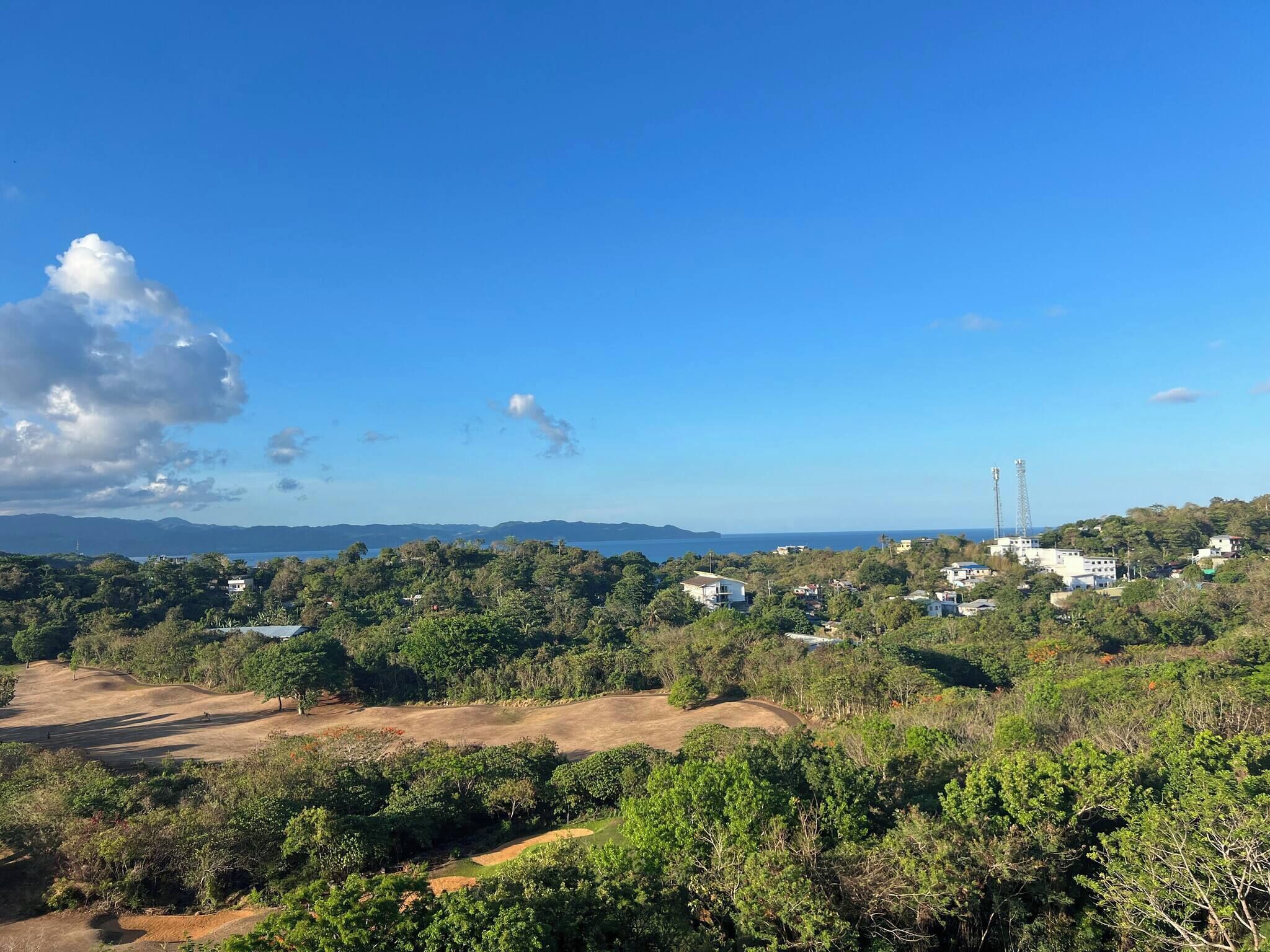 A coastal landscape with residential buildings, a golf course, and a clear blue sky.