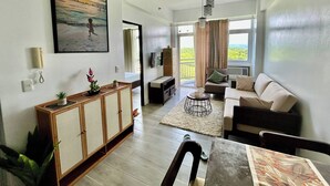 A modern living room with a sofa, a coffee table, a TV, and a balcony with a view. - Serene 1-Bedroom Apartment in Boracay with Pool Access (Boracay Island)