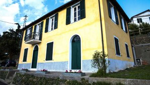 A yellow building with green shutters, a balcony, and a stone staircase. - Casa Nord Silvano - rustico di paese (Borghetto d'Arroscia)
