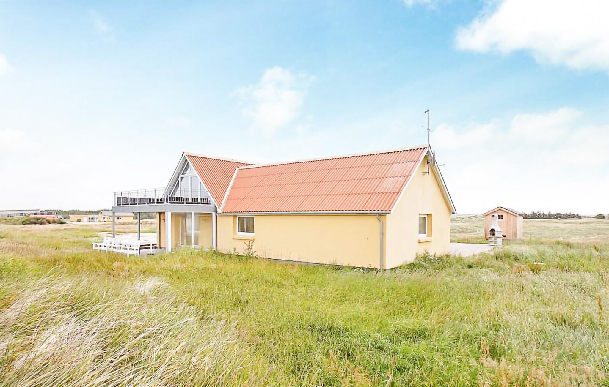 Un bâtiment d’un seul étage, avec un toit rouge, une petite construction attenante et un champ verdoyant au premier plan.