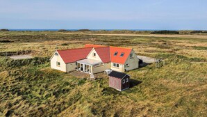 Una casa con techo rojo, un cobertizo pequeño adosado y un campo de césped al fondo.