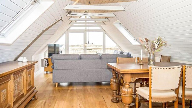 Un apartamento estilo loft con techo de madera, un sofá gris, una mesa de comedor de madera con sillas y un televisor al fondo.