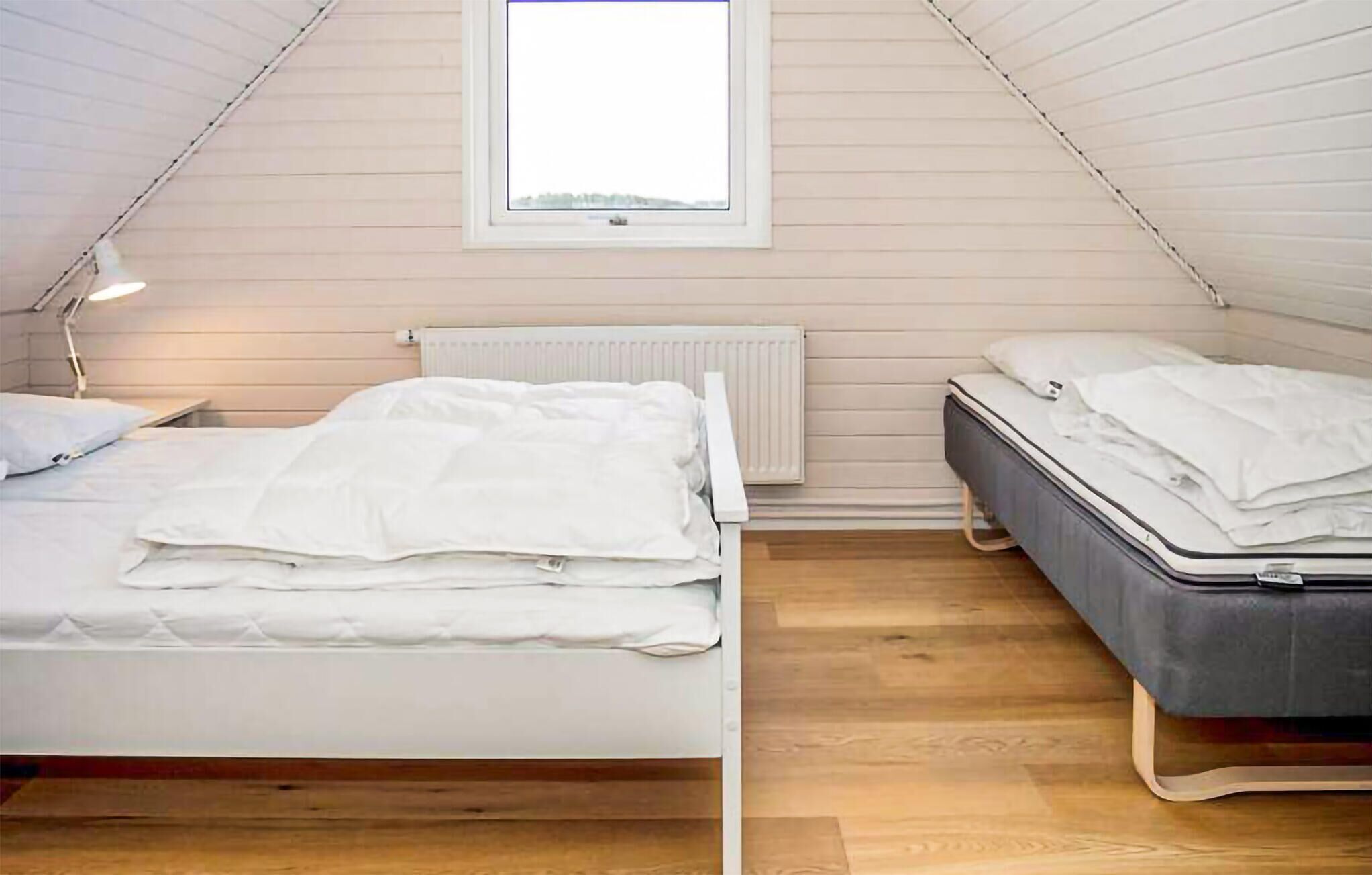 Quarto com duas camas, janela, radiador e abajur.