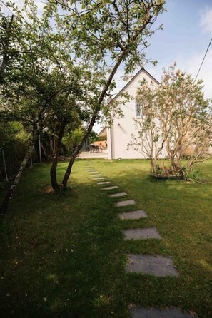 A pathway leading to a white building with a sloped roof, surrounded by trees and a well-maintained lawn. - Maison "Lomy" bord de mer- 2ch- Large enclosed garden (Pléneuf-Val-André)