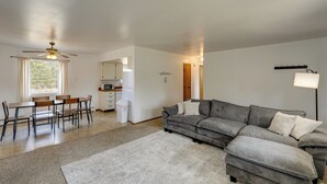 Un salon moderne avec un canapé d’angle, une table à manger, des chaises, un ventilateur de plafond et, au fond, un coin cuisine.