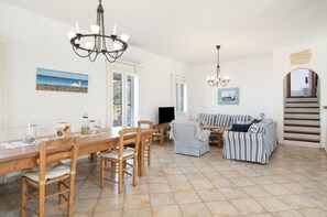 A dining area with a wooden table and chairs, a sofa, and a chandelier.