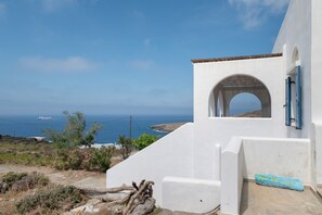 Ein weißes Gebäude mit blauer Tür, einem steinernen Bogen und Blick aufs Meer.