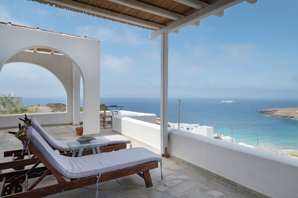 A balcony with lounge chairs, a table, and a view of the sea.
