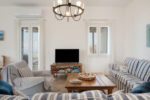 A living room with a television, a wooden coffee table, striped sofas, and a chandelier.