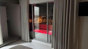 Una habitación moderna con una puerta de cristal que da a un balcón, un sofá rojo y un televisor de pantalla plana en la pared.