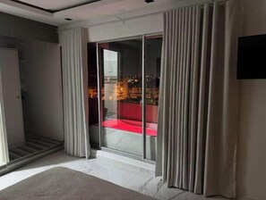 Ein modernes Zimmer mit Glastür zum Balkon, einem roten Sofa und einem Flachbildfernseher an der Wand.