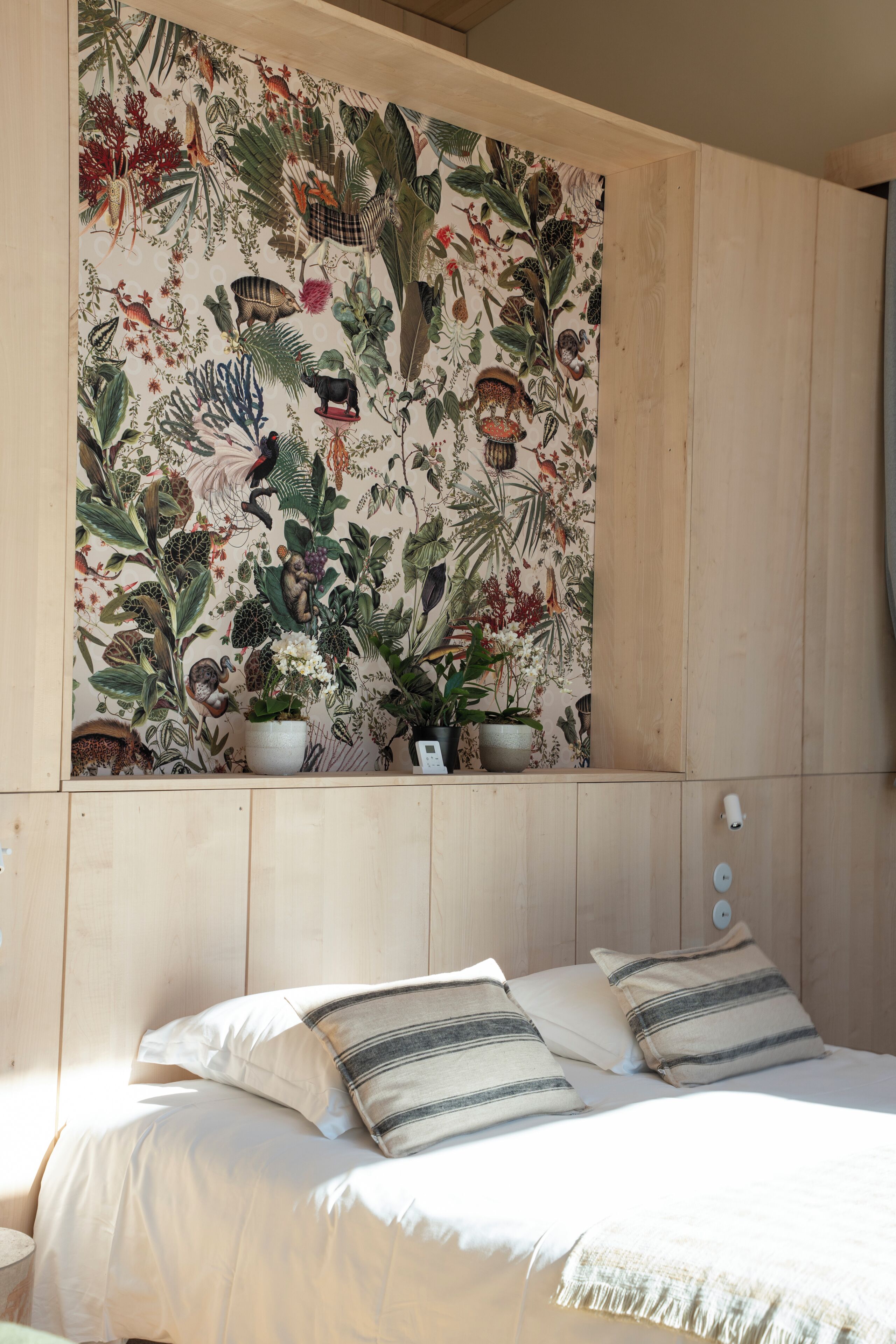 Ein Schlafzimmer mit Bett, Kissen, einer Wand mit Pflanzenprint und Topfpflanzen.