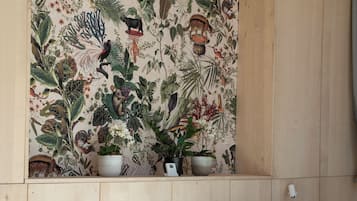 Un dormitorio con cama, almohadas, un cuadro botánico en la pared y plantas en macetas.