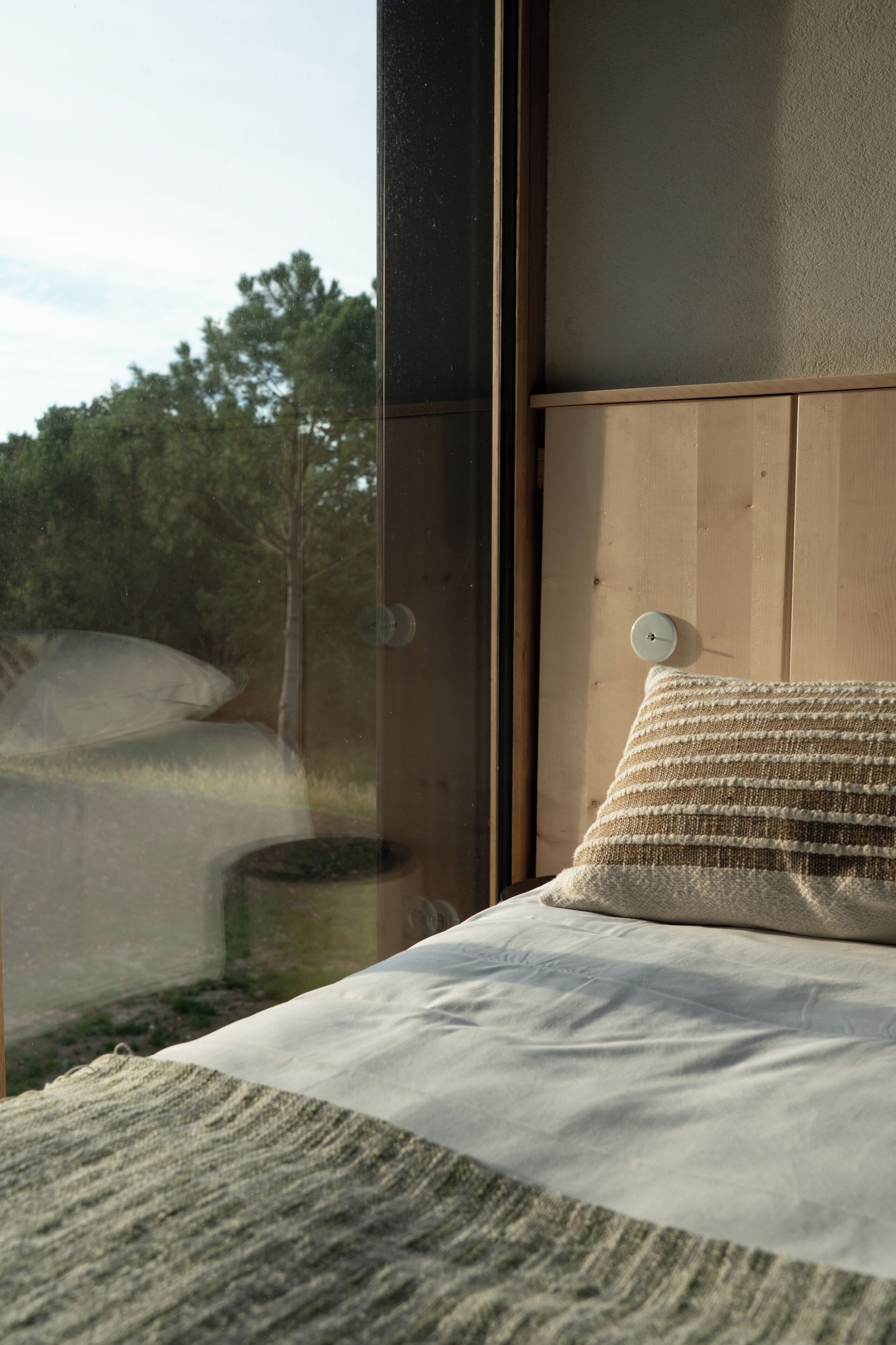 Ein Schlafzimmer mit großem Fenster, einem Holz-Kopfteil und einem einzelnen Kissen.