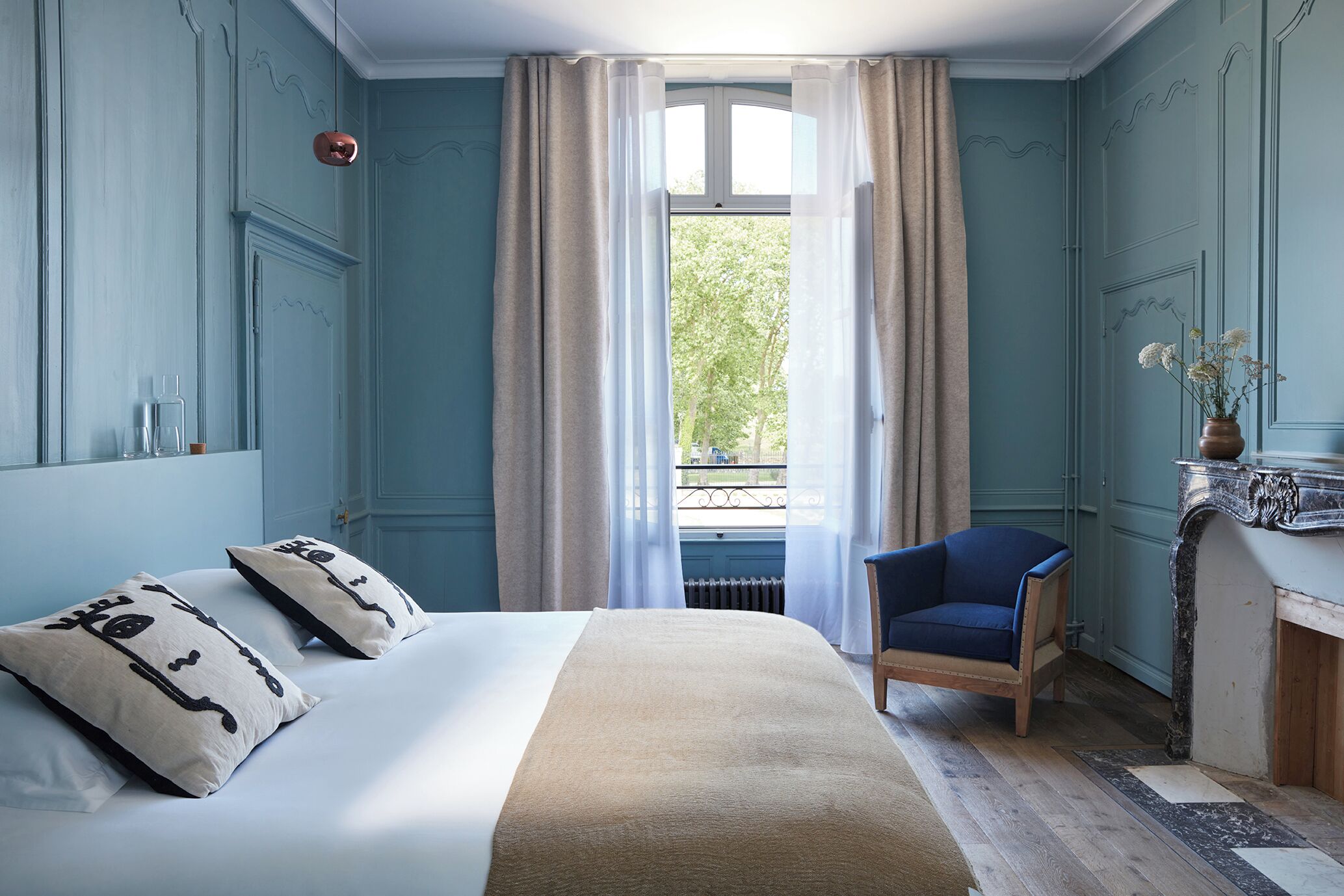 Ein Schlafzimmer mit Bett, Stuhl, Vorhängen am Fenster und Kamin.