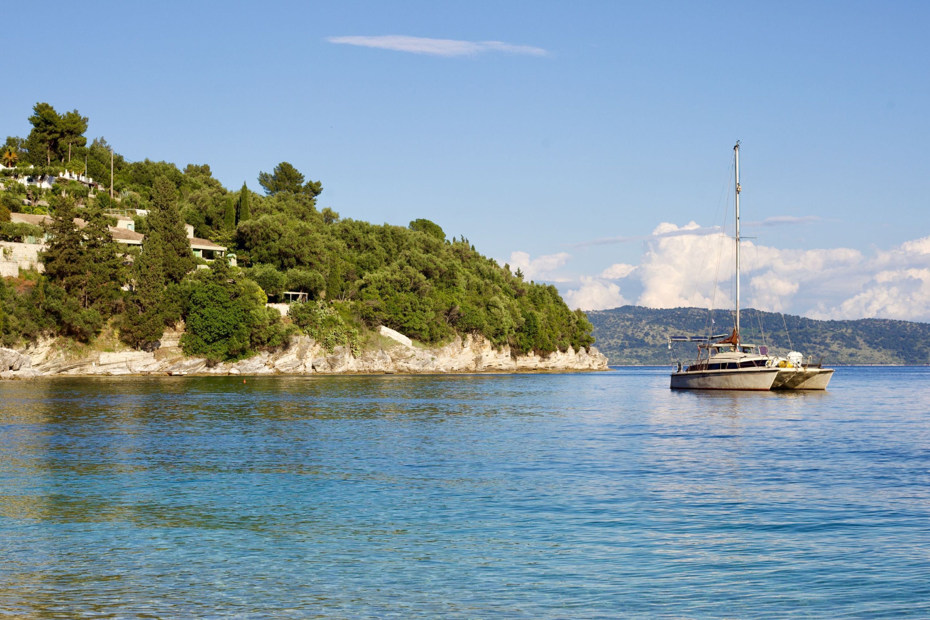 A calm body of water with a boat anchored near a hillside with buildings.