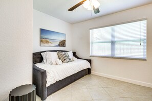 Ein Zimmer mit einem Bett, einem Gemälde, einem Fenster mit Jalousien und einem Deckenventilator.
